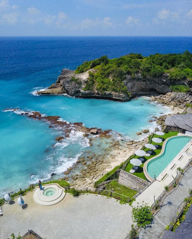 Aerial view of the Blue Lagoon cove on Nusa Ceningan, with a cliff-top pool and loungers beside it